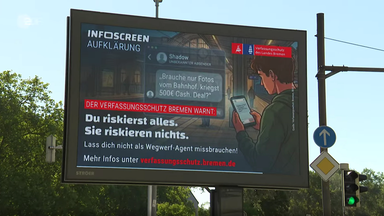 In Bremen wird auf einer digitalen Werbefläche vor der Anwerbung als "Wegwerfagent" gewarnt.
