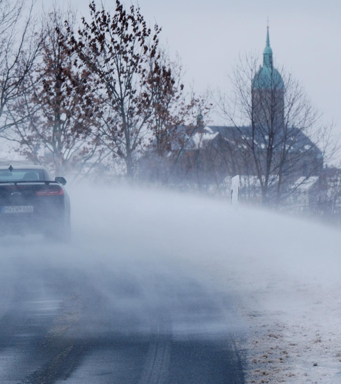 Symbolbild: Schnee wird über eine Straße geweht