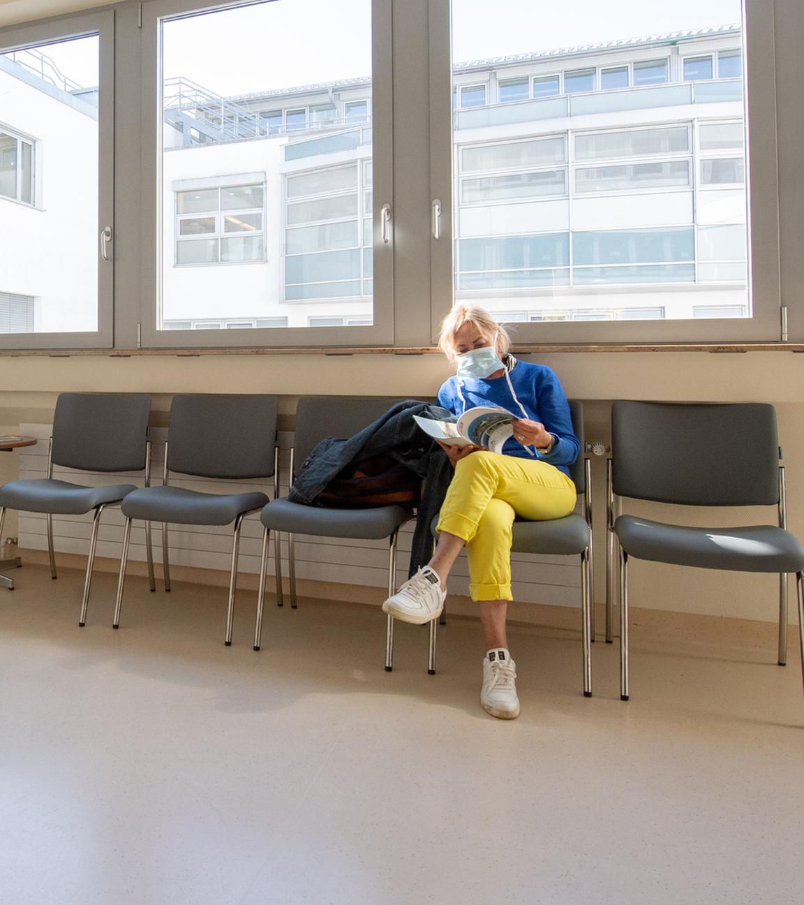 Eine Patientin mit Mundschutz wartet in einem ansonsten leeren Wartebereich in einer Klinik in Gauting bei München.