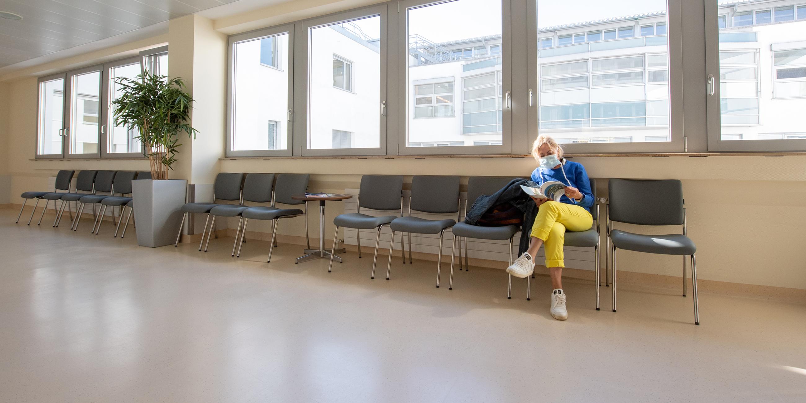 Eine Patientin mit Mundschutz wartet in einem ansonsten leeren Wartebereich in einer Klinik in Gauting bei München.