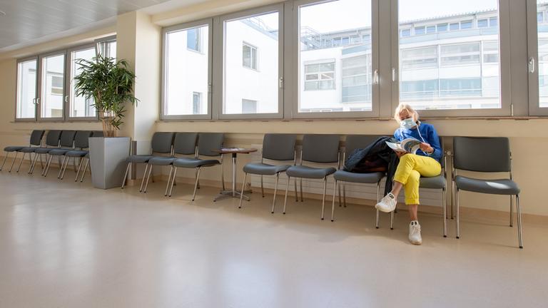 Eine Patientin mit Mundschutz wartet in einem ansonsten leeren Wartebereich in einer Klinik in Gauting bei München.