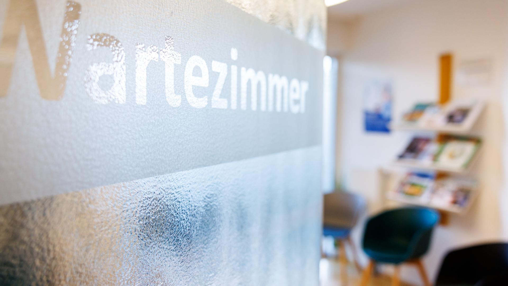 Auf einer Glastür die in ein Wartezimmer führt, steht der Schriftzug "Wartezimmer". (Symbolbild)