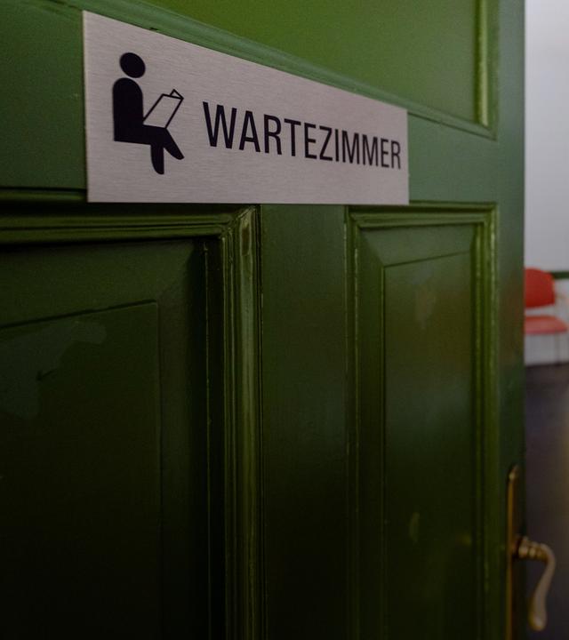 An der Tür einer Arztpraxis ist das Wort 'Wartezimmer' zu lesen.