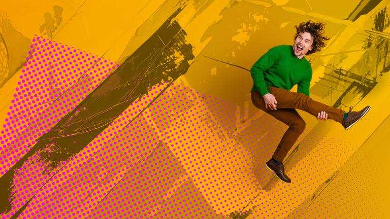 Mann, der in die Luft springt und mit einem seiner Beine eine Gitarre simuliert.