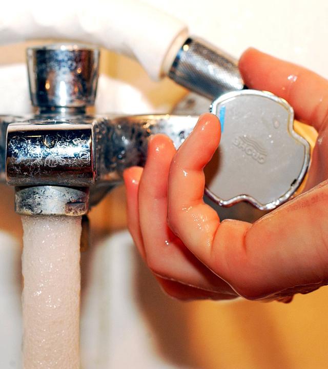 Hand dreht an Wasserhahn.