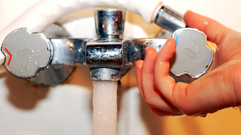 Hand dreht an Wasserhahn.