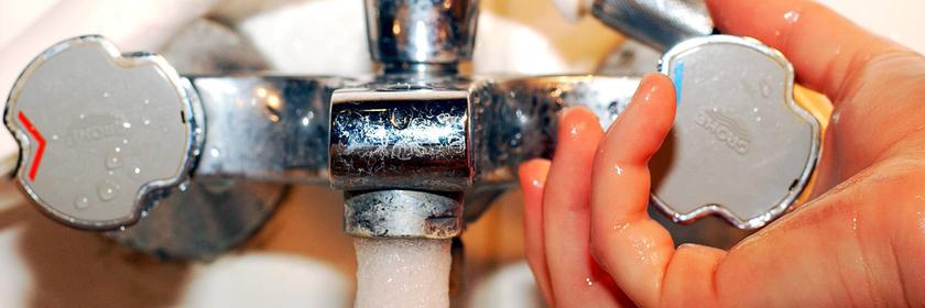 Hand dreht an Wasserhahn.
