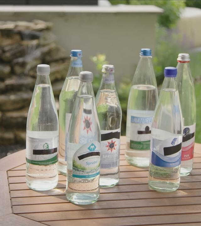 Viele Wasserflaschen unterschiedlicher Marken stehen auf einem Beistelltisch.