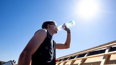 Ein Mann steht in der prallen Sonne und trinkt Wasser aus einer Plastikflasche.