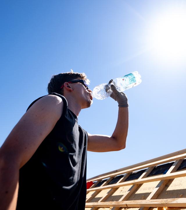 Ein Mann steht in der prallen Sonne und trinkt Wasser aus einer Plastikflasche.