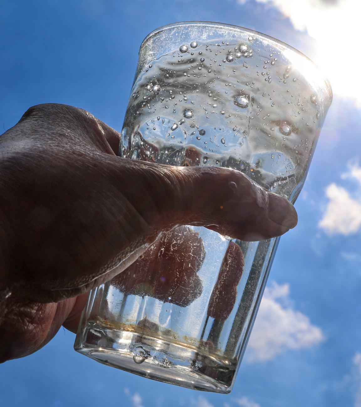Ein mit Mineralwasser gefülltes Glas wird gegen das Sonnenlicht gehalten.