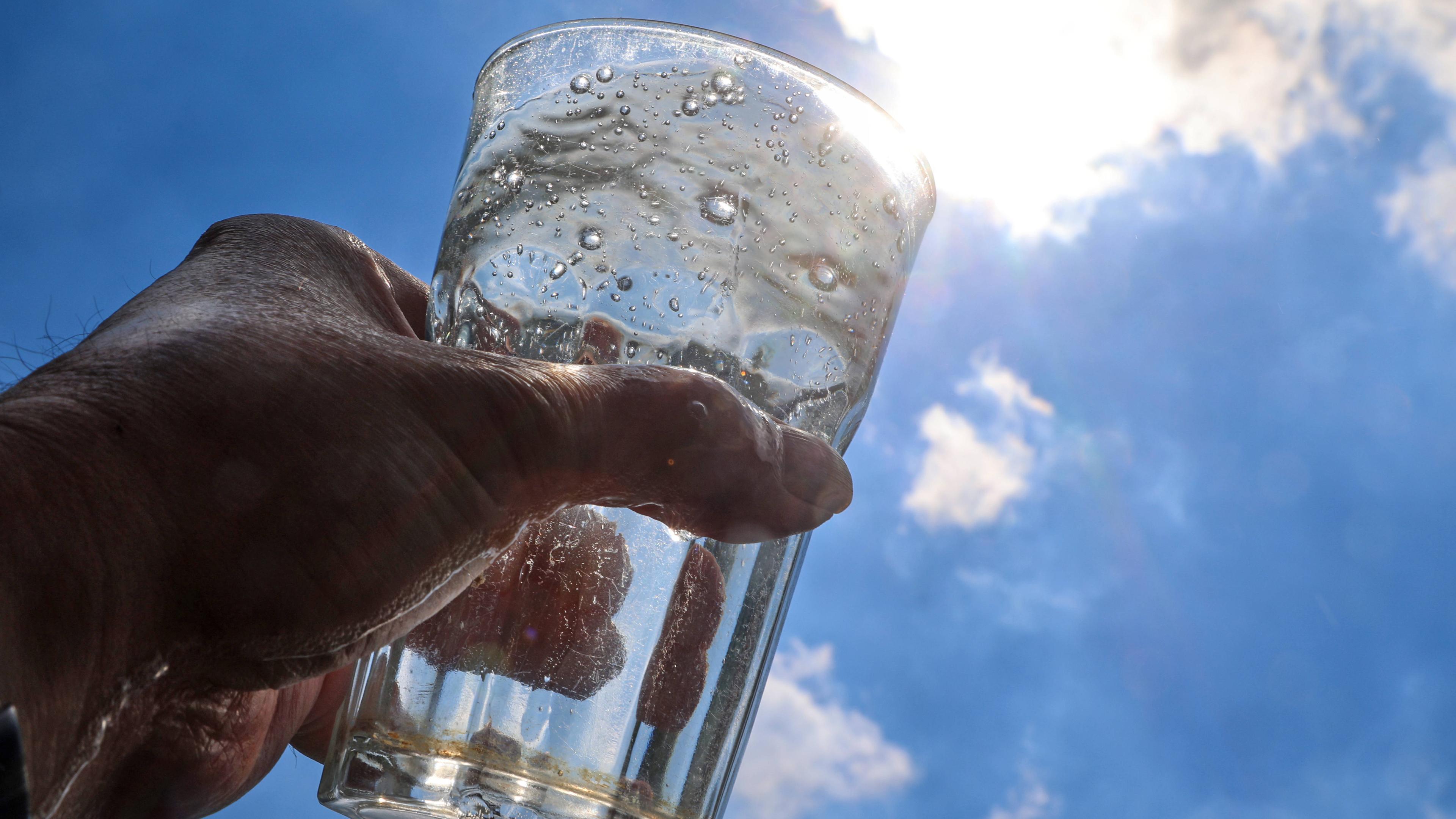 Ein mit Mineralwasser gefülltes Glas wird gegen das Sonnenlicht gehalten.