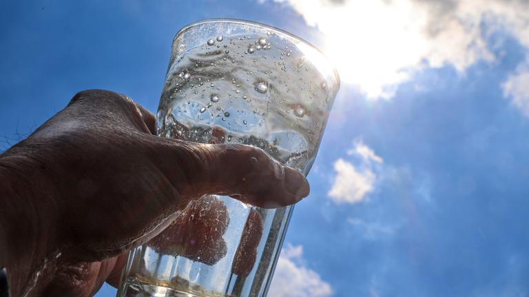 Ein mit Mineralwasser gefülltes Glas wird gegen das Sonnenlicht gehalten.
