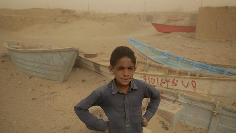 Ein Junge steht vor alten und zurückgelassenen Booten, wo einst ein See war.