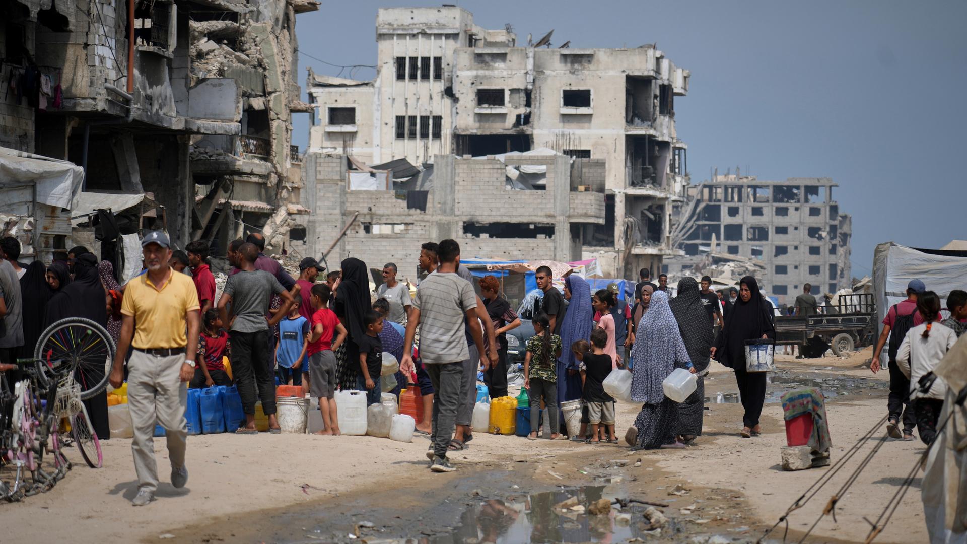 In der Sommerhitze stellen sich Palästinenser an, um Wasser an einer Verteilungsstelle in Gaza zu holen.
