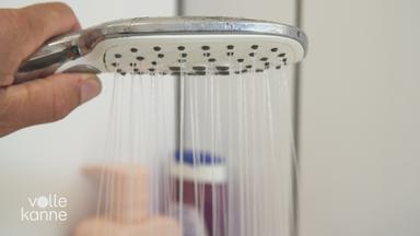 Eine Person hält einen Duschkopf, aus dem Wasser kommt