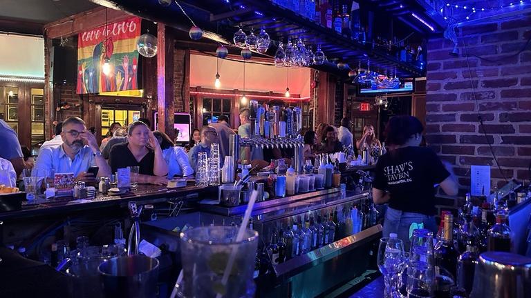 Menschen sitzen an einem Tresen und fassen sich an den Kopf.