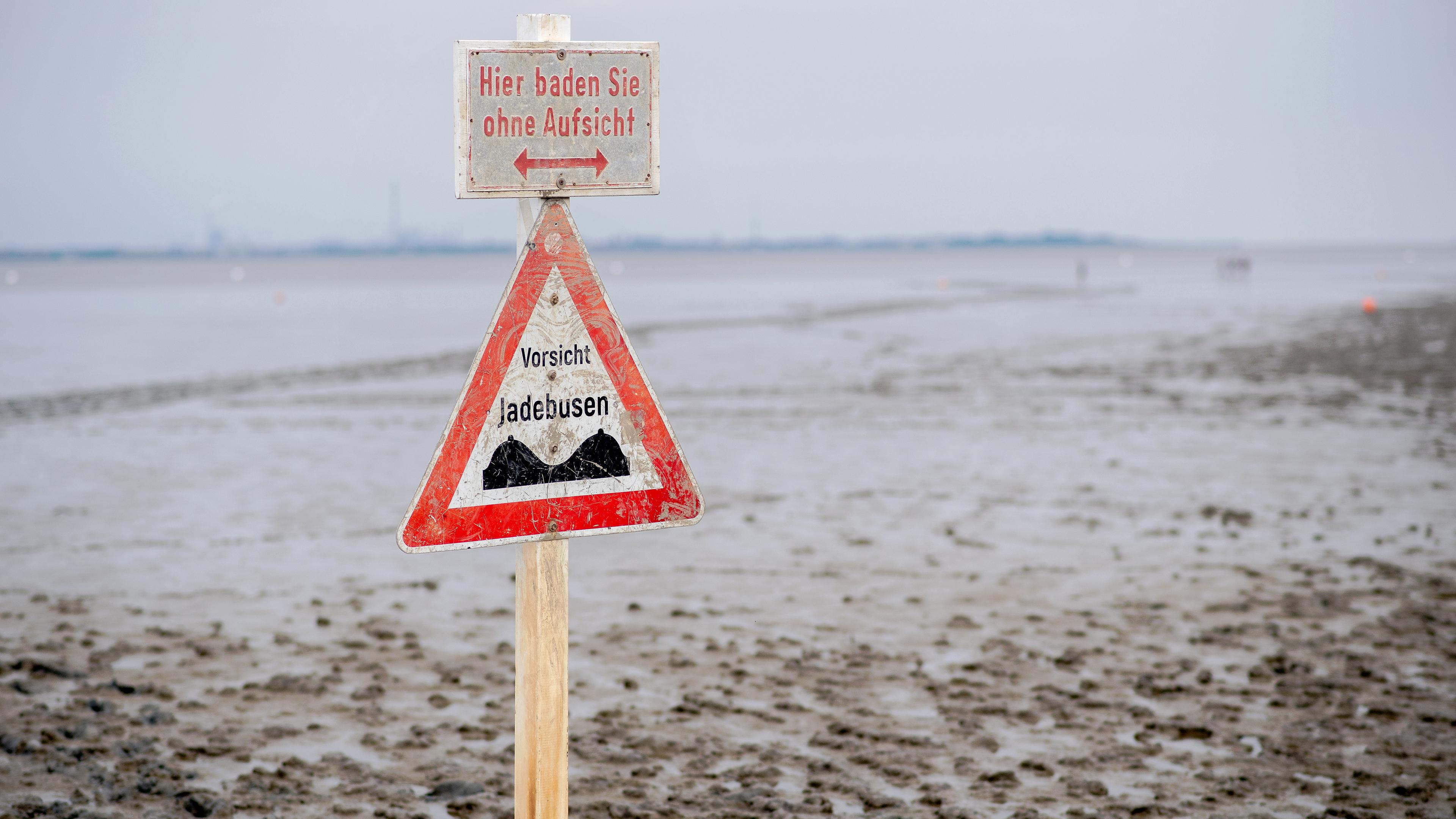 Ein Schild mit der Aufschrift ·Vorsicht Jadebusen· steht im Wattboden am Strand von Dangast
