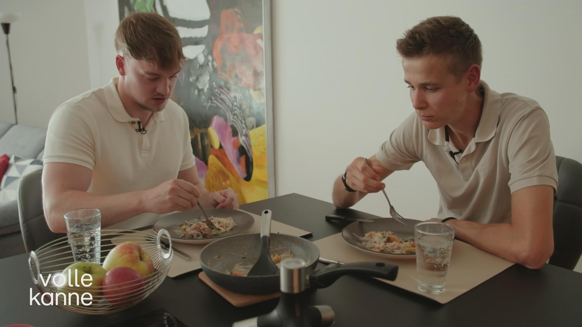 Zwei Männer sitzen am Tisch und essen.