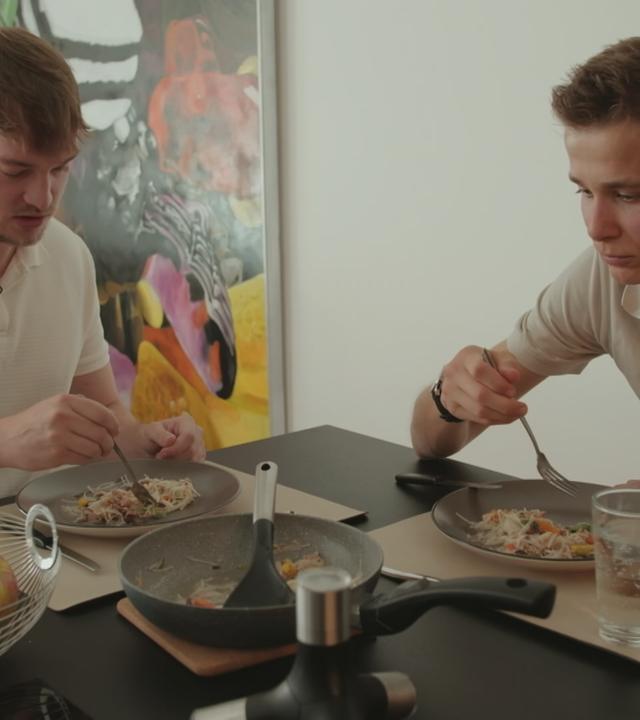Zwei Männer sitzen am Tisch und essen.
