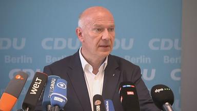 Kai Wegner ist während einer Konferenz zu sehen. Mehrere Mikrofone sind auf ihn gerichtet.