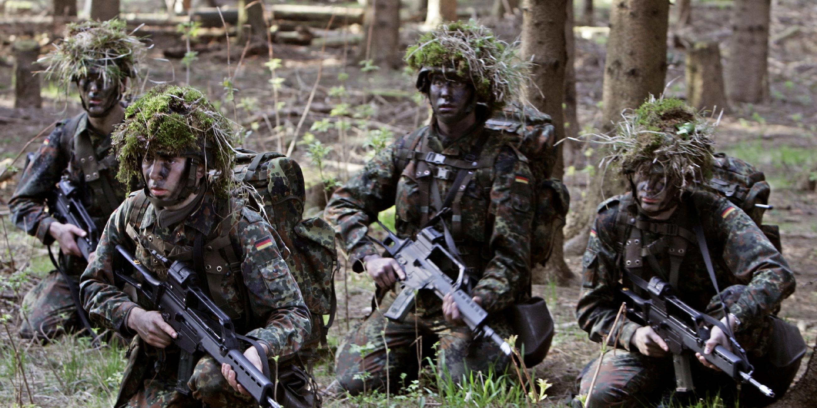 Mit Ballwerk und Gras betarnte Wehrpflichtige mit Gewehren während einer Geländeübung im Wald.