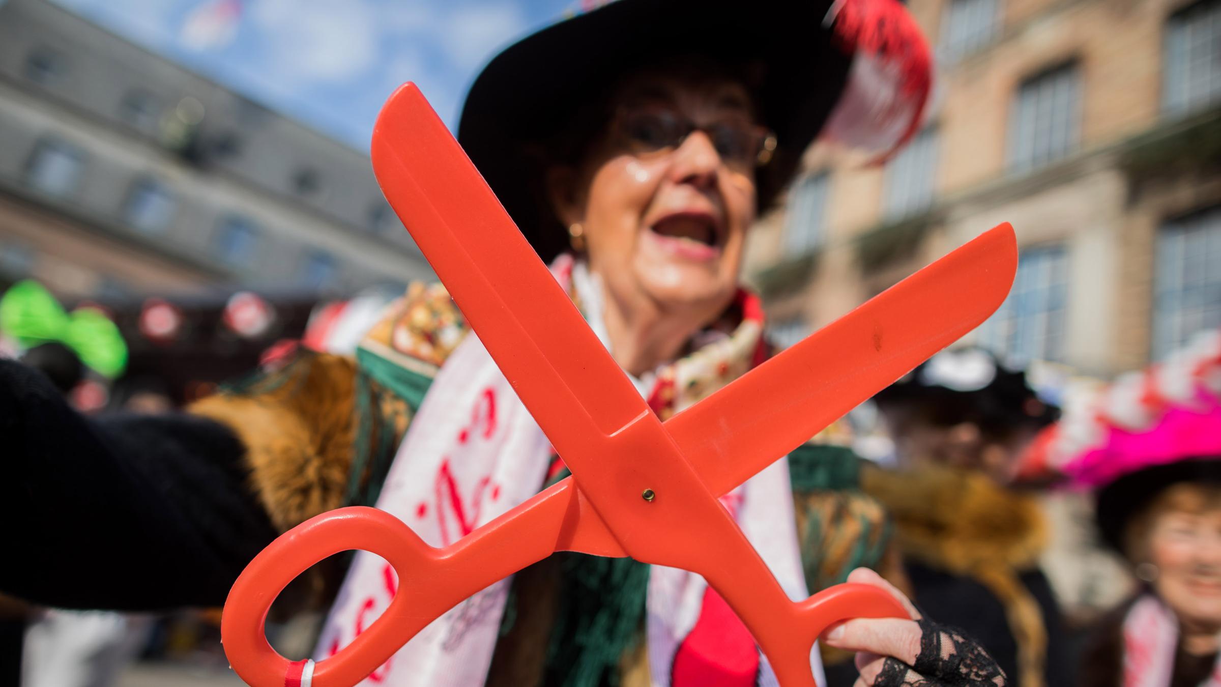 Eine Frau mit einer großen Schere steht vor dem Düsseldorfer Rathaus.