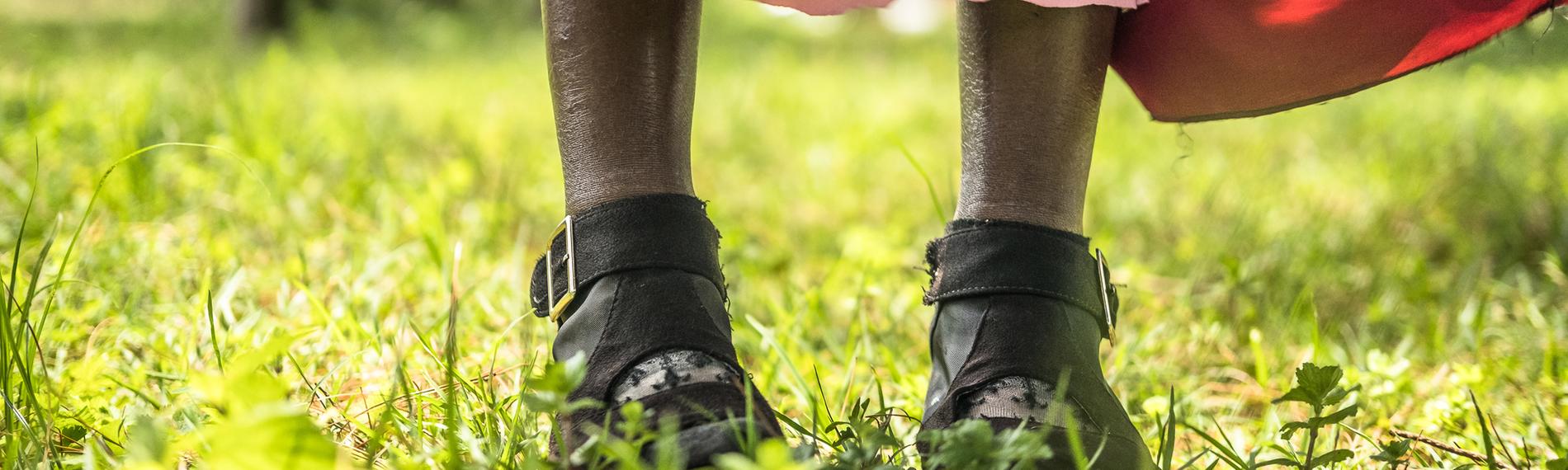 Eine Frau steht auf einer Wiese, man sieht nur ihr Knöchel und das untere Ende ihres Kleids