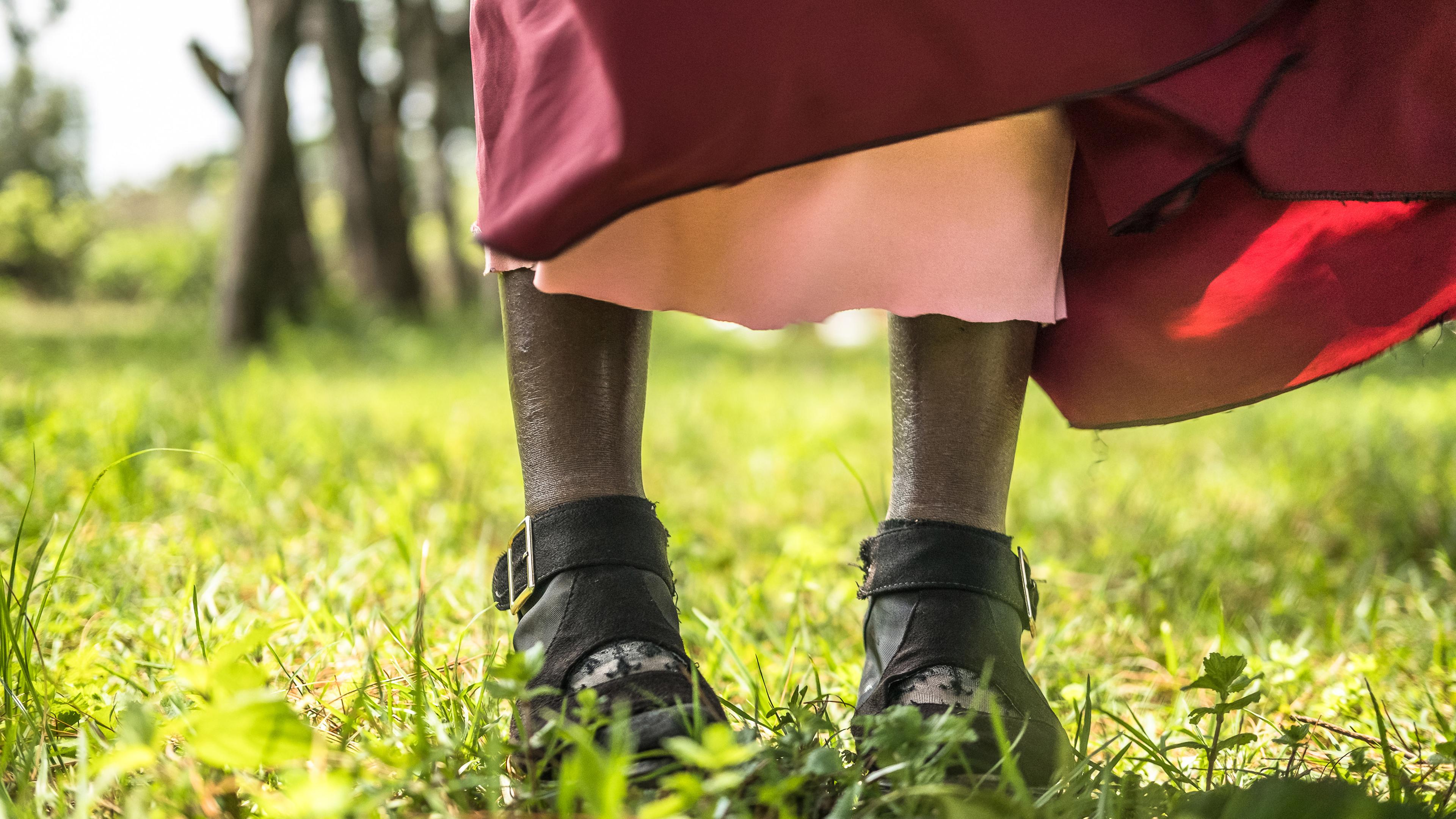 Eine Frau steht auf einer Wiese, man sieht nur ihr Knöchel und das untere Ende ihres Kleids