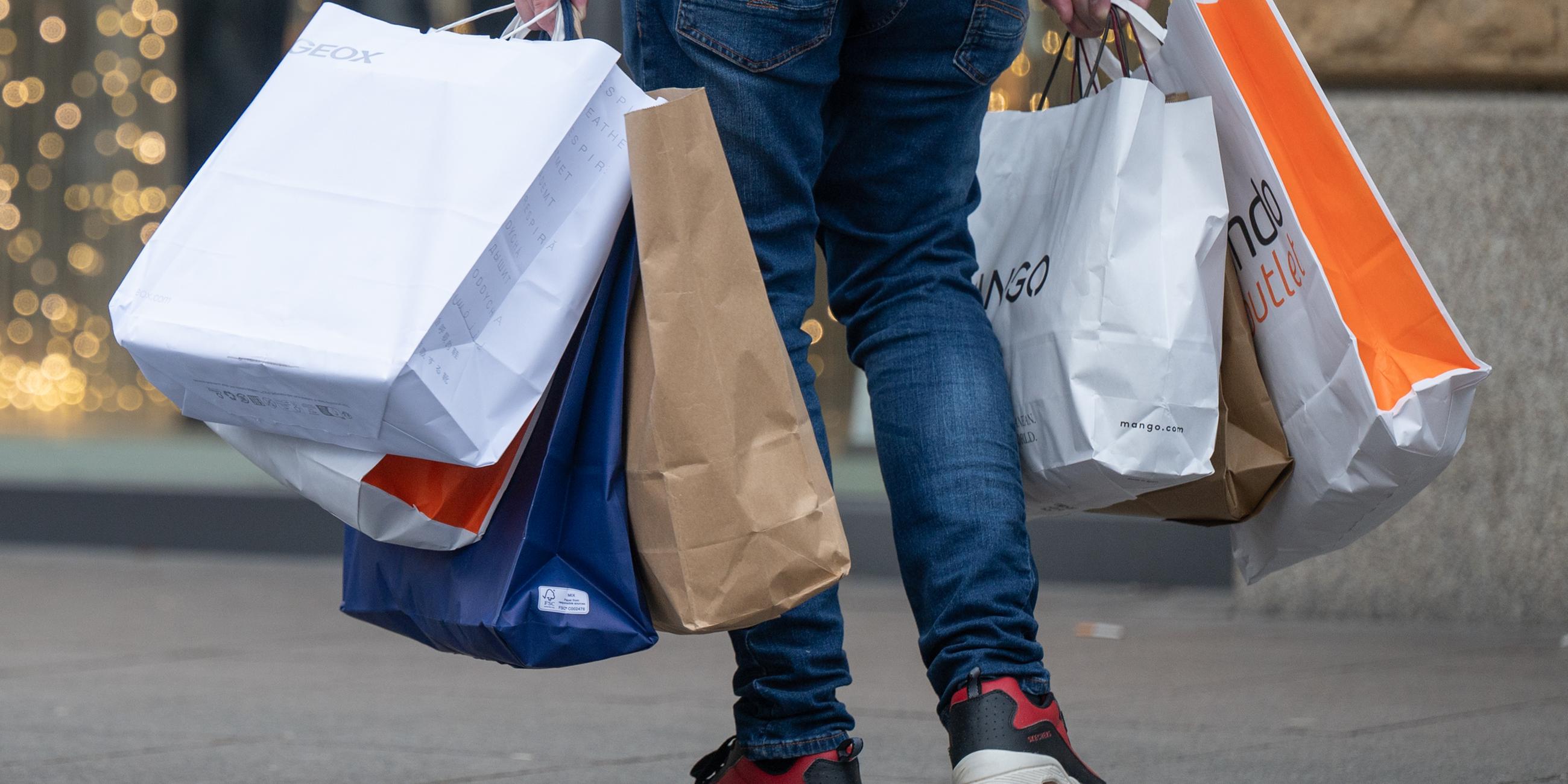 Mit vollen Einkaufstüten in den Händen geht ein Mann über einen Weg.