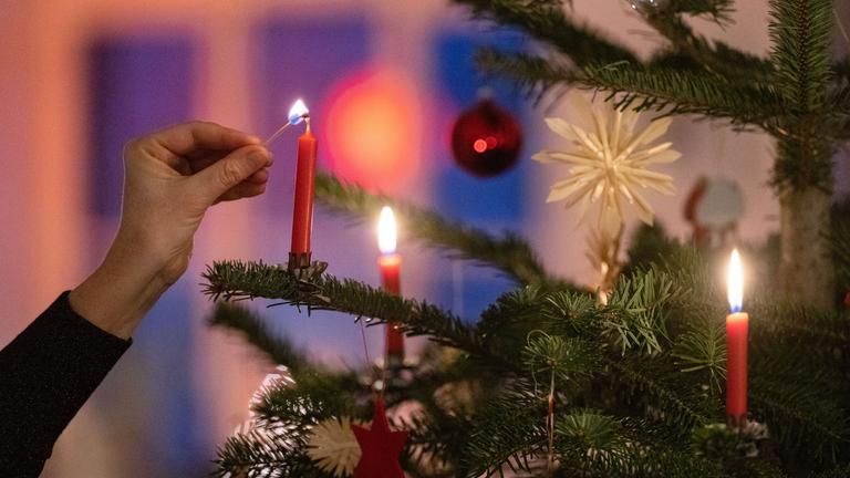 Eine Kerze wird an einem geschmücktem Weihnachtsbaum angezündet.