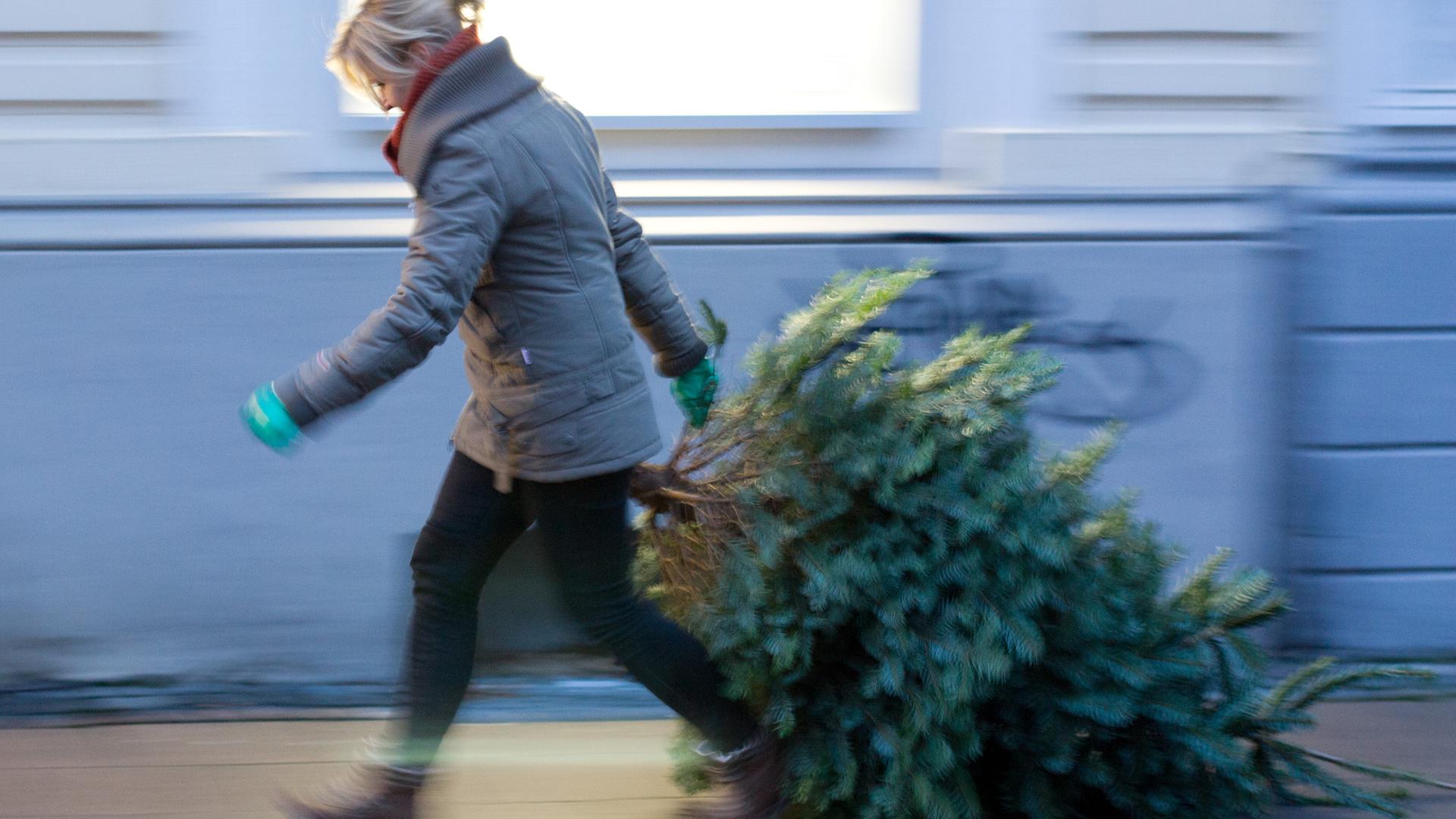 Frau bringt Weihnachtsbaum auf die Straße.
