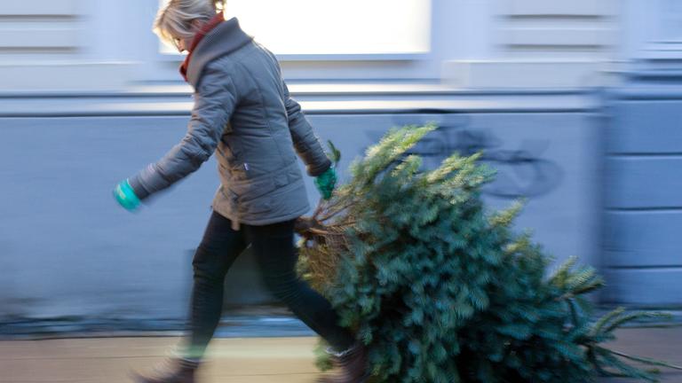 Frau bringt Weihnachtsbaum auf die Straße.