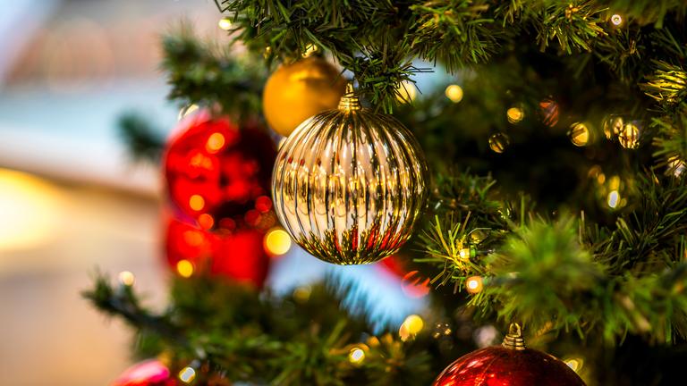 Eine goldene Weihnachtskugel hängt an einem geschmückten Christbaum.