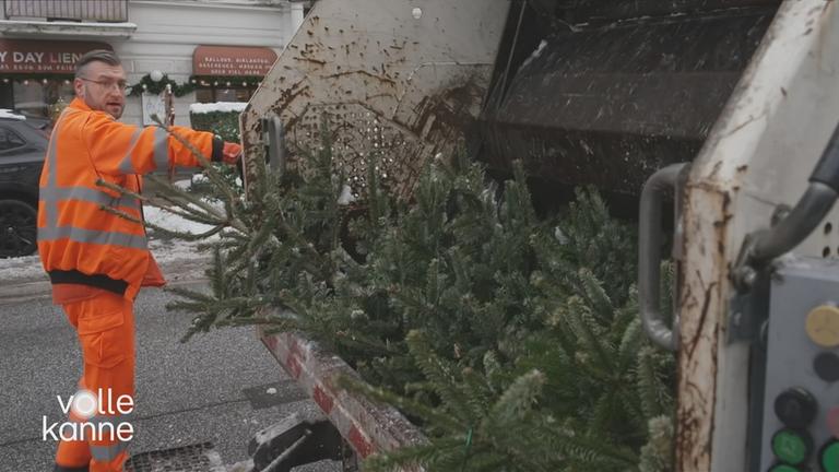 Ein Mann der Müllabfuhr lädt die Tannenbäume in die Müllpresse rein.