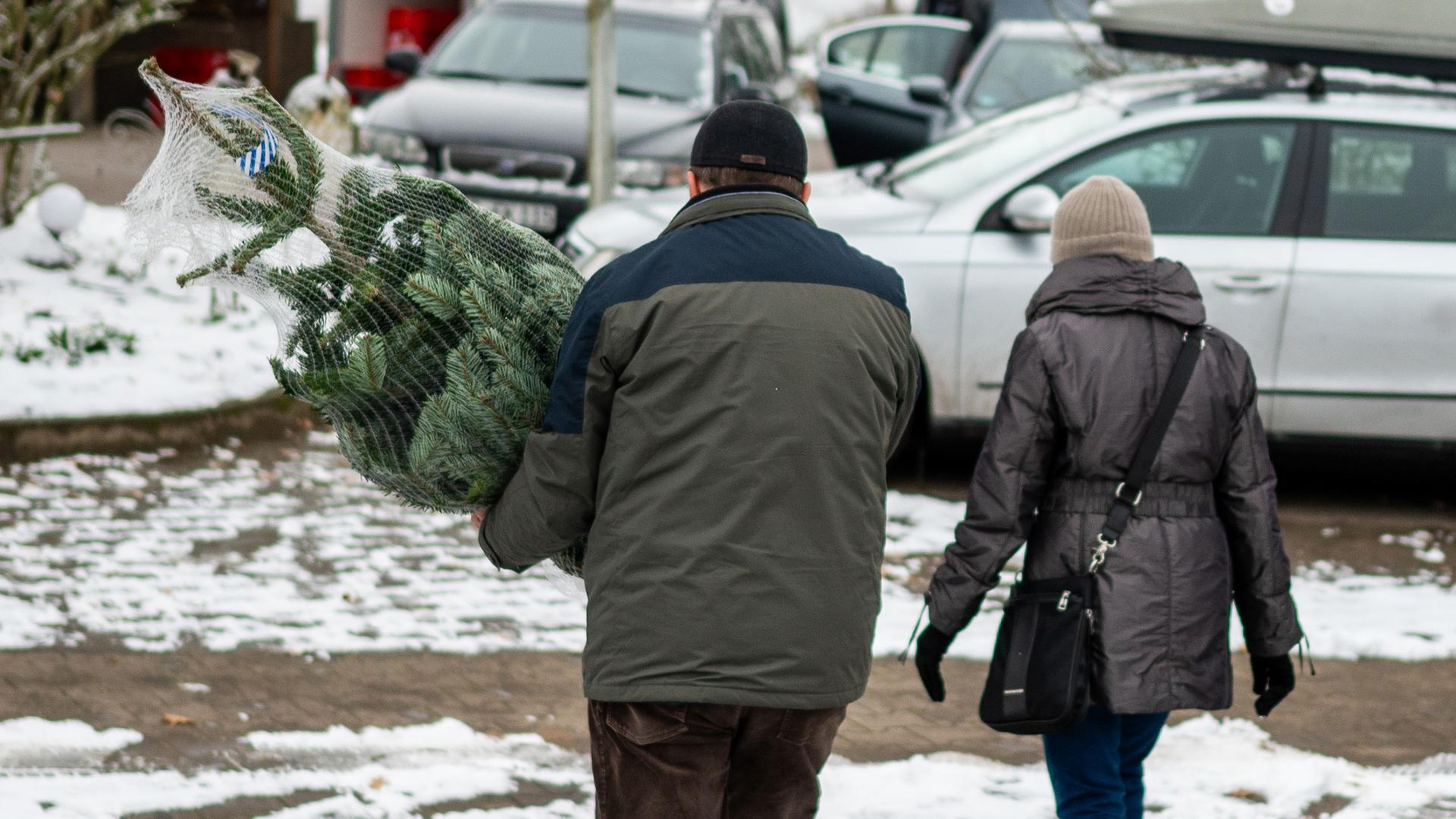 Zwei Kunden gehen mit eigenem Weihnachtsbaum zum Auto. 