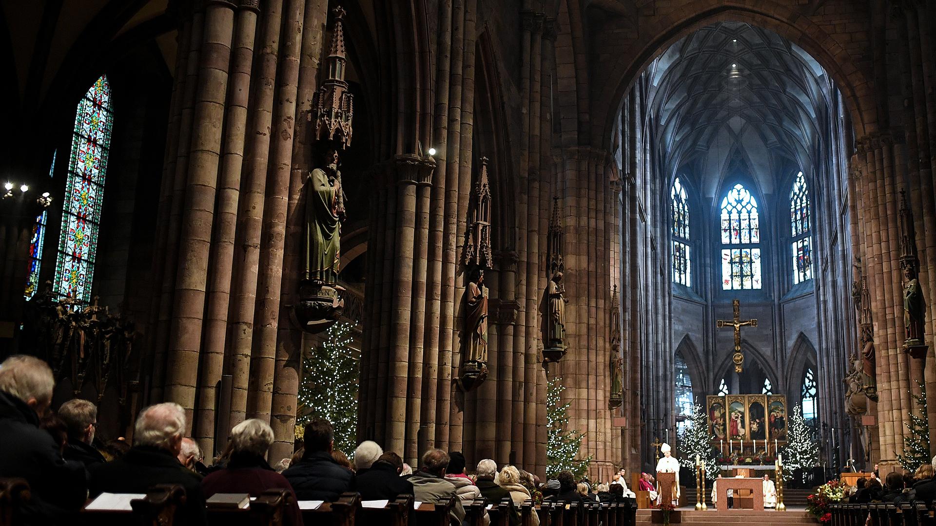 Kirchenbesucher hören im Münster beim Pontifikalamt zu Weihnachten der Predigt von Erzbischof Stephan Burger zu.