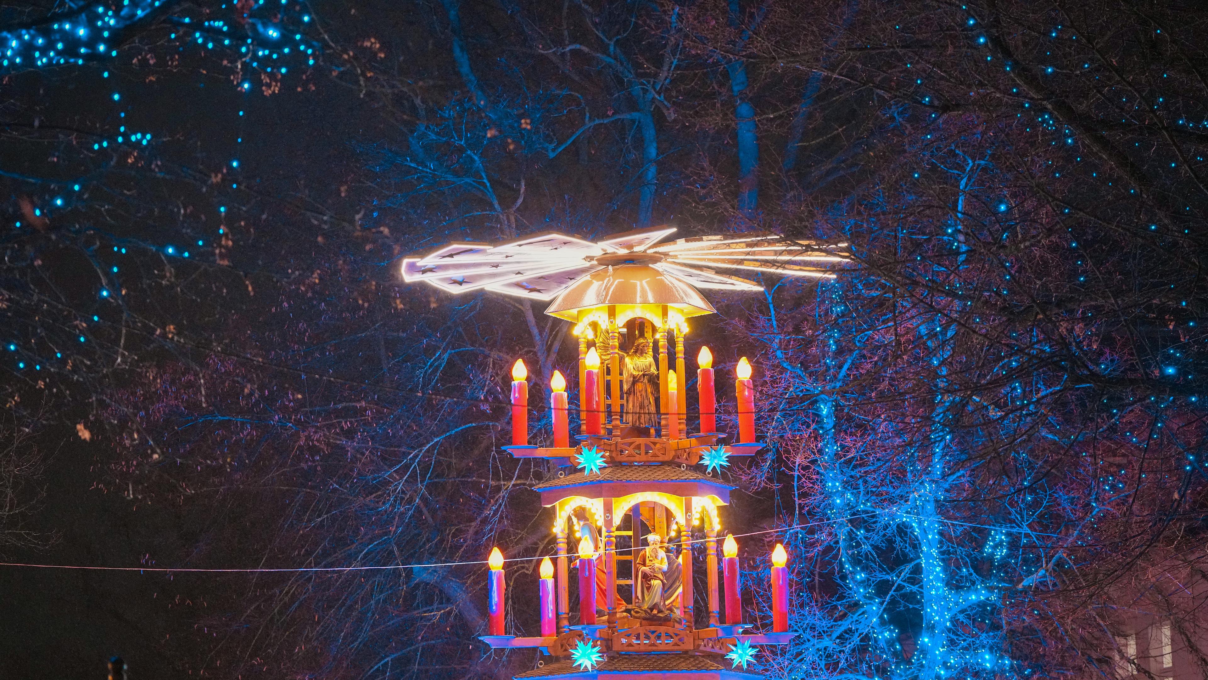 Eine beleuchtete Pyramide steht während des Potsdamer Weihnachtsmarktes "Blauer Lichterglanz" in Potsdam vor einem blau beleuchteten Baum. 