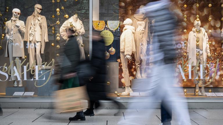 Menschen eilen in der Einkaufsstraße «Zeil» an einem festlich geschmückten Schaufenster vorbei, das mit «SALE» und winterlicher Dekoration für das Weihnachtsgeschäft wirbt.