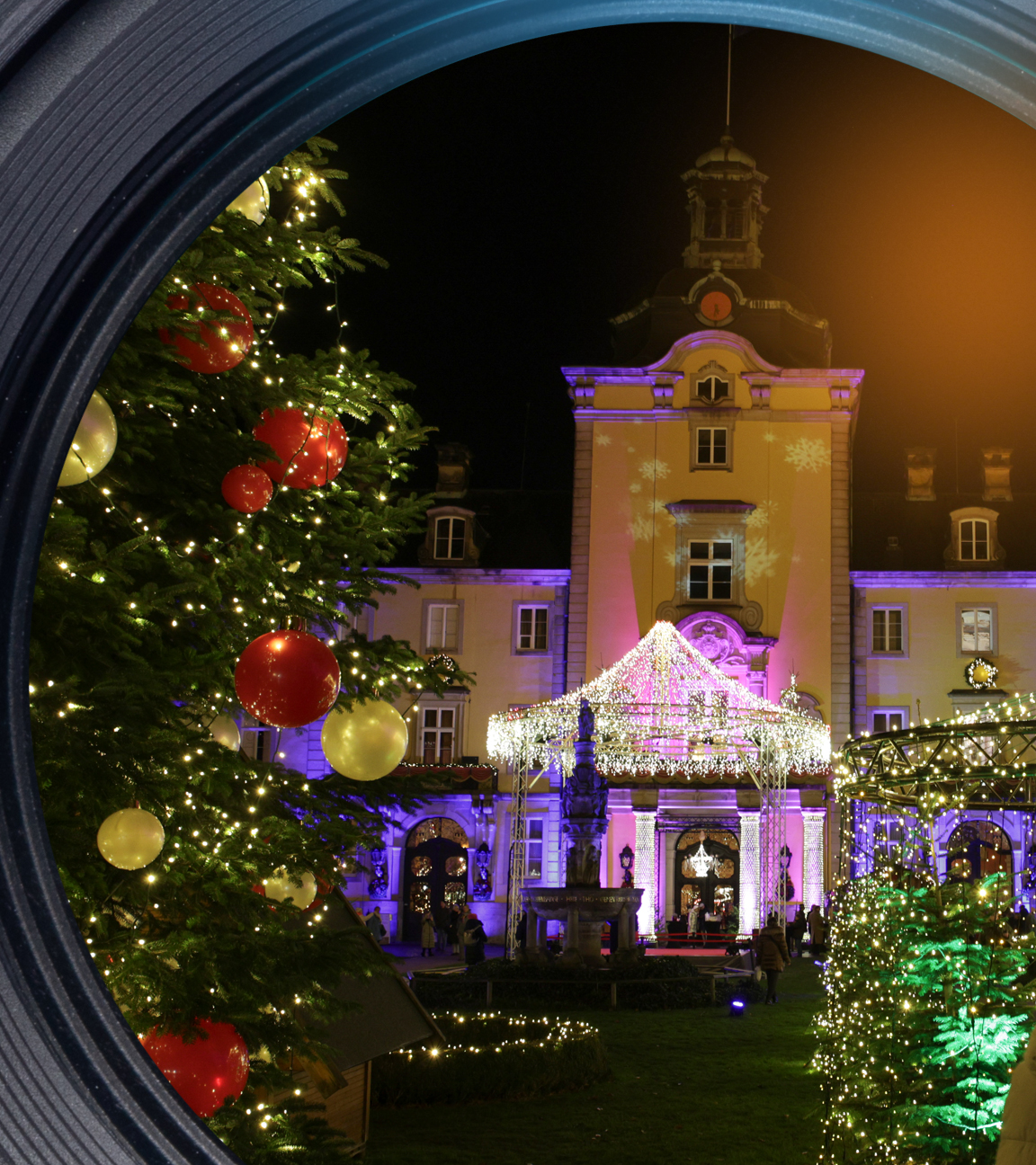 Ein Weihnachtsbaum und viele Lichter auf einem Weihnachtsmarkt auf einem Schloss.