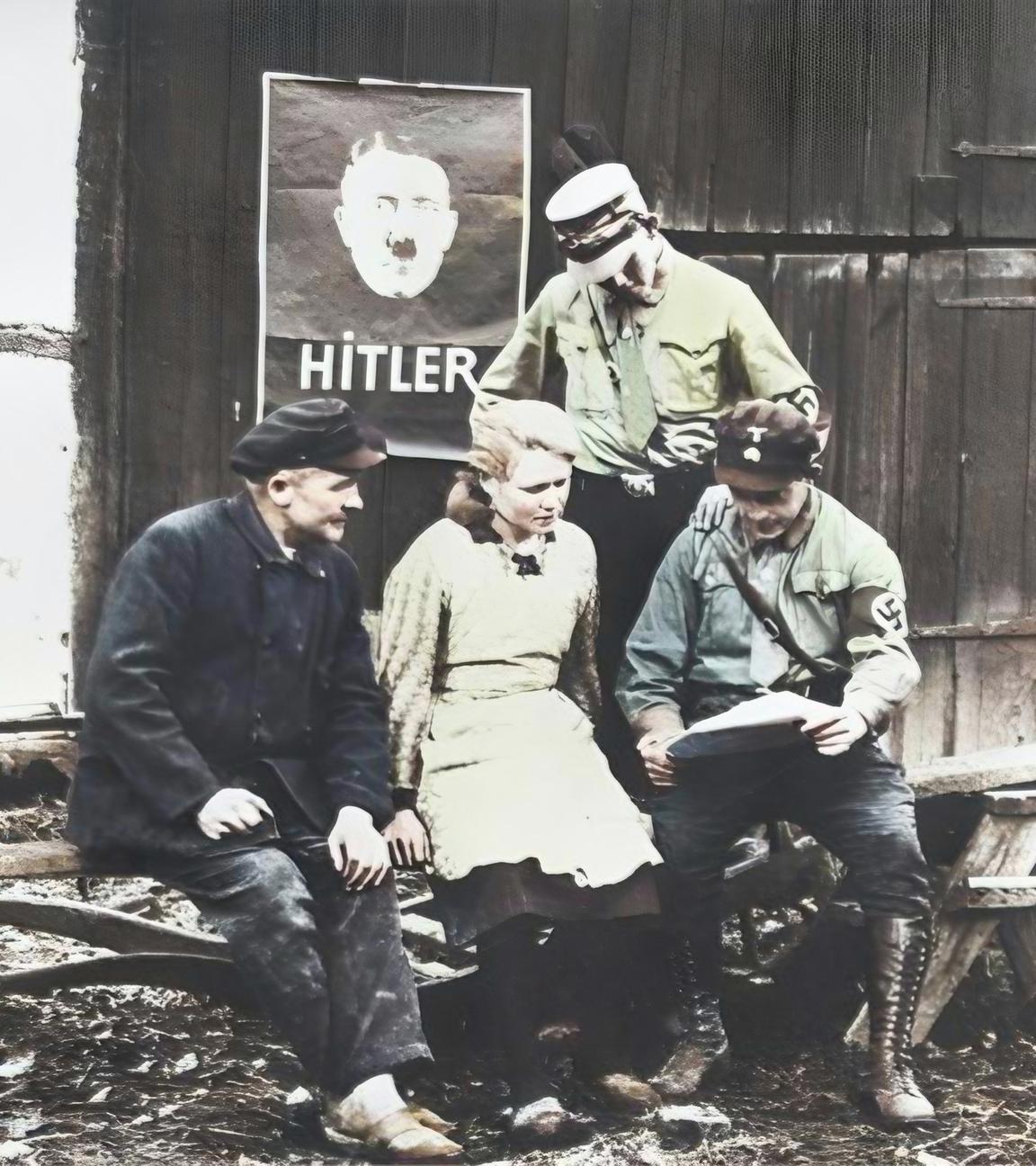 In der Weimarer Republik sitzen und stehen fünf Wähler vor einem Holztor mit einem Werbeplakat, auf dem Adolf Hitler abgebildet ist.