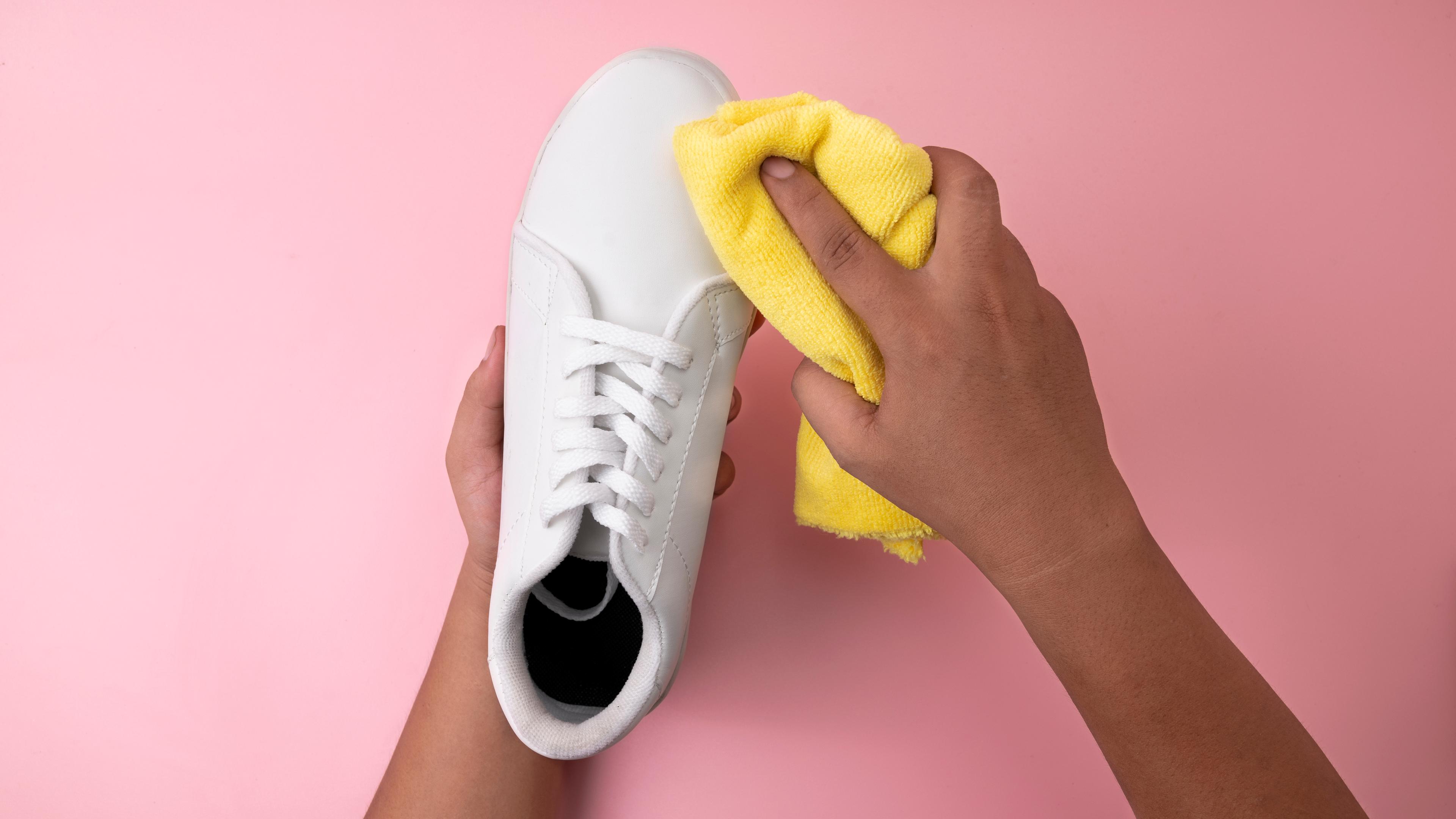Ein weißer Sneaker wird mit einem Mikrofasertuch gereinigt.