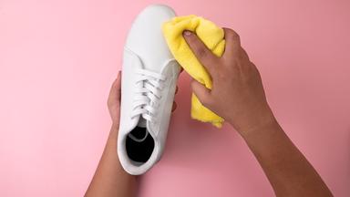 Ein weißer Sneaker wird mit einem Mikrofasertuch gereinigt.
