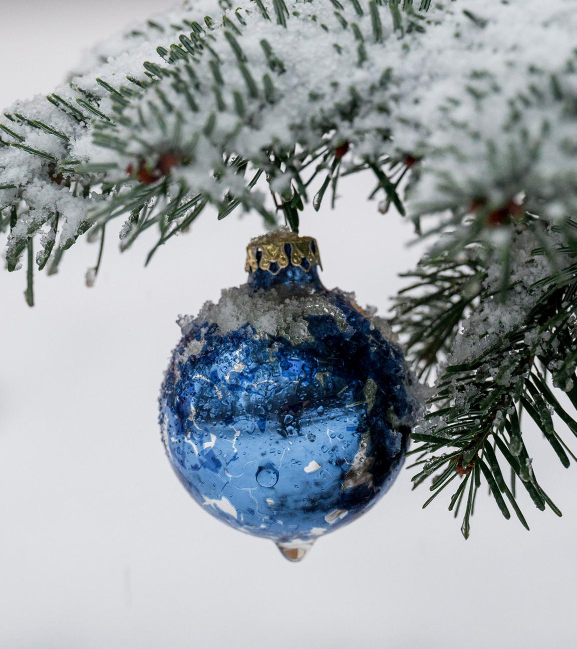 Eine Christbaumkugel hängt in einem schneebedeckten Weihnachtsbaum. (Symbolbild)