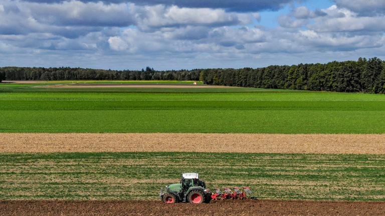 Ein Mann mit einem Traktor pflügt einen Acker (Aufnahme mit Drohne). 