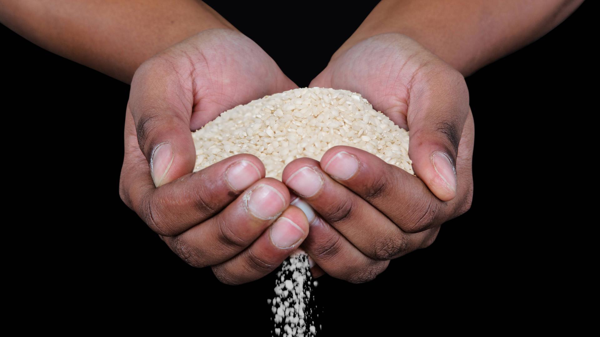 Symbolbild: Eine Hand voll Reis fließt durch die Hände