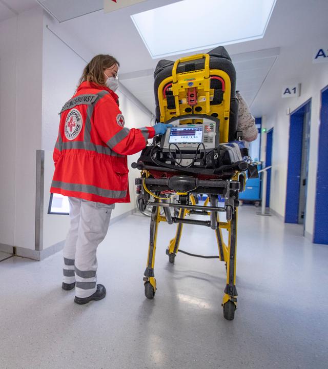 Miriam Görg, Notfallsanitäterin des Deutschen Roten Kreuzes (DRK), schiebt eine Seniorin nach einem Schlaganfall auf einer Trage in die Notaufnahme eines Krankenhauses und wartet auf die Übergabe an die diensthabende Ärztin.