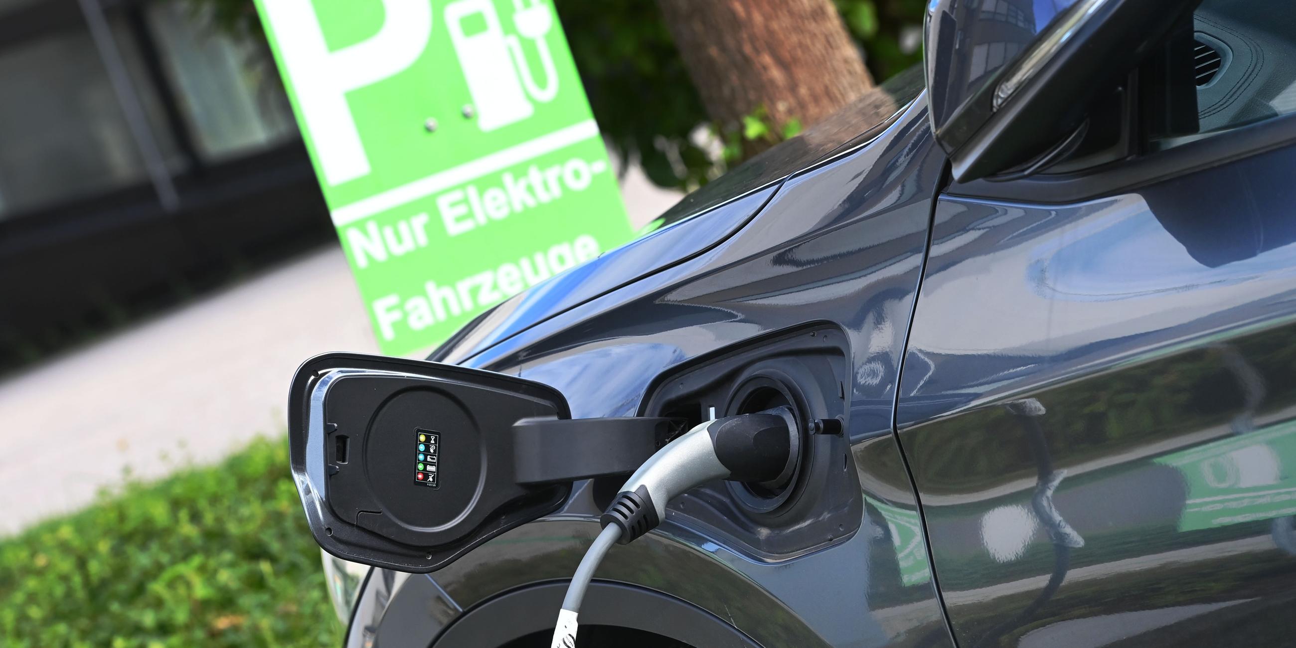 E-Auto wird auf einem Parkplatz nur fuer Elektro-Fahrzeuge geladen,Stecker waehrend dem Ladevorgang an einem E-Auto