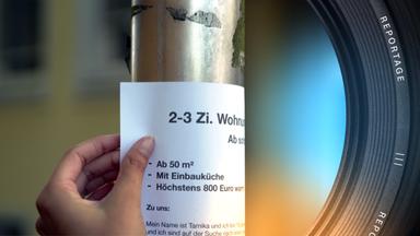 Eine Person befestigt einen Wohnungsgesuchszettel an einer metallenen Stange.