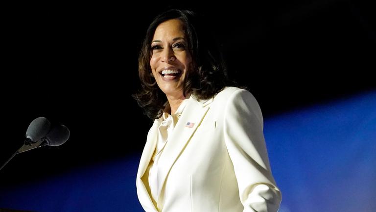 Kamala Harris steht an einem Rednerpult. Sie lächelt. 